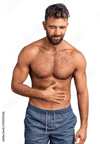 Young hispanic man wearing swimwear shirtless with hand on stomach because indigestion, painful illness feeling unwell. ache concept.