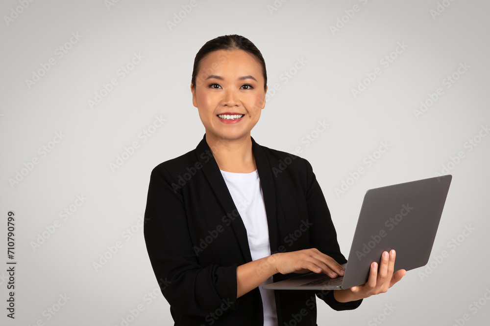 A confident young Asian businesswoman in a black blazer and white top holds an open laptop A confident young Asian businesswoman in a black blazer and white top holds an open laptop