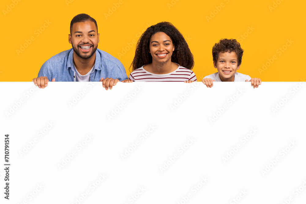 Offer for families. Black parents and son leaning on white advertisement board Offer for families. Black parents and son leaning on white advertisement board