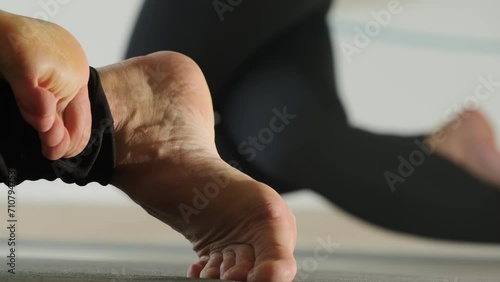 Woman maintains crossed legs position with bare feet on floor in gym. Heels of woman off ground during exercise in yoga studio closeup photo