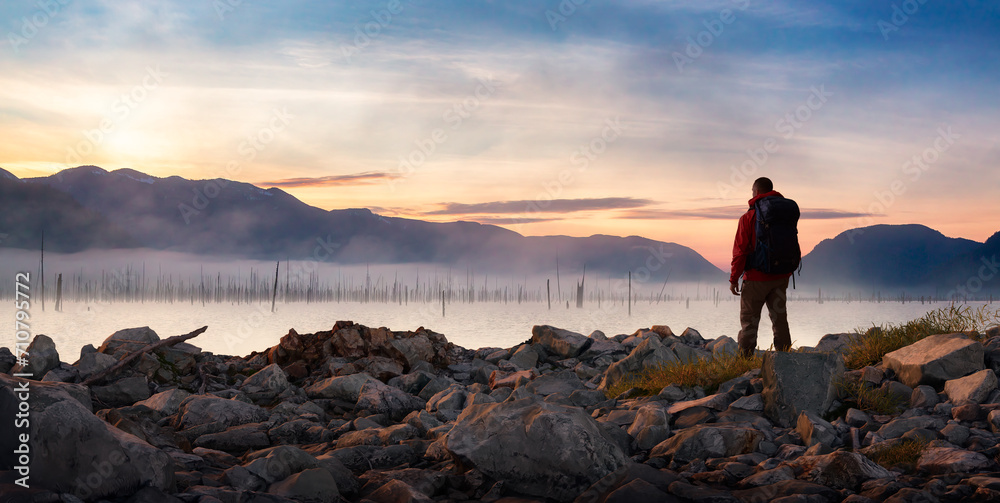 Adventure Man standing on rocky shore by the lake with mountains in background. 3d Rendering.