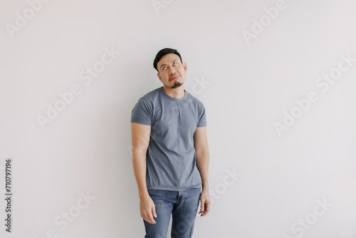 Disappointed and bored face of asian man in blue t-shirt stand isolated on white wall.