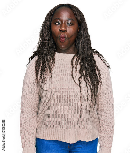 Young african woman wearing wool winter sweater making fish face with lips, crazy and comical gesture. funny expression.