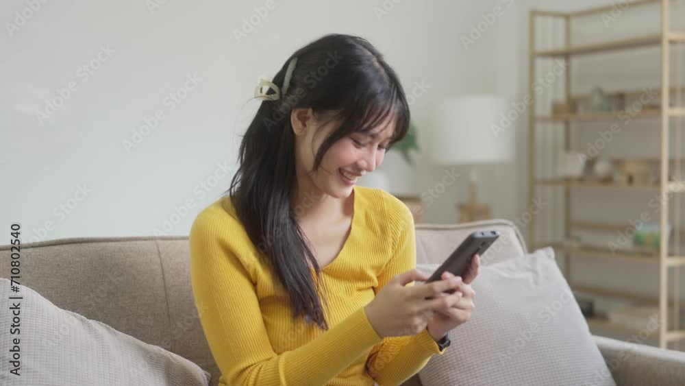 Asian Woman using cell phone sitting on couch.. Asian Woman using cell phone sitting on couch..