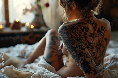 Sexy beautiful young slender woman with a tattoo on her back sitting on bed. Back view of an erotic blonde in bedroom photo