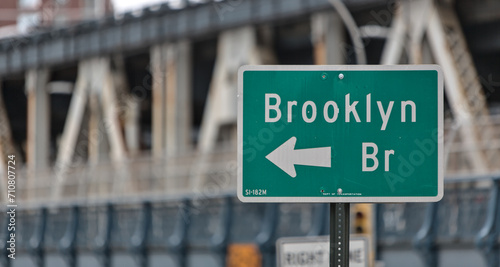 brooklyn bridge sign on the side of the road in downtown brooklyn, new york city (famous landmark travel destination signage in nyc) isolated close up out of focus manhattan bridge background photo