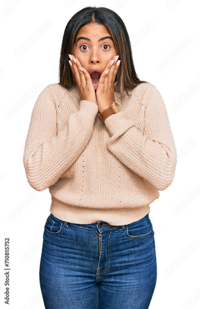 Young latin girl wearing wool winter sweater afraid and shocked, surprise and amazed expression with hands on face Young latin girl wearing wool winter sweater afraid and shocked, surprise and amazed expression with hands on face