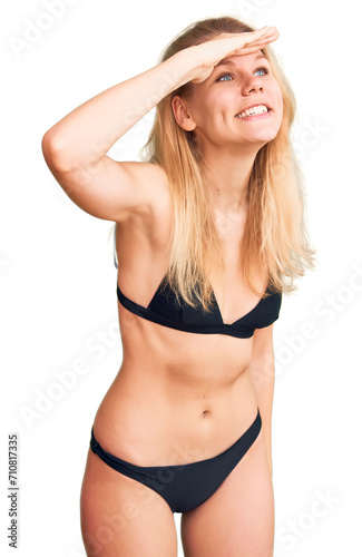 Young beautiful blonde woman wearing bikini very happy and smiling looking far away with hand over head. searching concept.