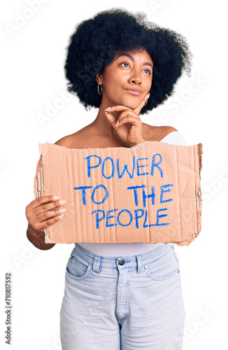 Young african american girl holding power to the people banner serious face thinking about question with hand on chin, thoughtful about confusing idea © Krakenimages.com