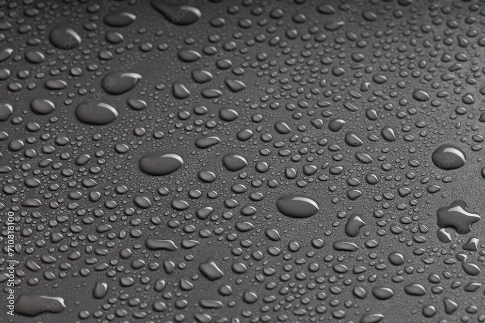 top view of a black surface with water droplets of various shapes