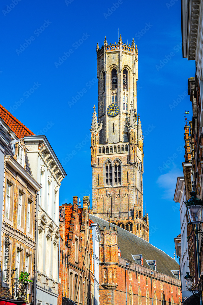 Belfry of Bruges Belfort van Brugge medieval bell tower behind old buildings in Brugge old town Steenstraat quarter, Bruges city historical centre, vertical view, West Flanders province, Belgium