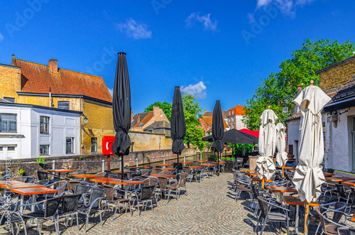 Street restaurant with tables and chairs on embankment of Green water canal in Brugge old town district, medieval houses buildings in Bruges city historical centre, West Flanders province, Belgium photo
