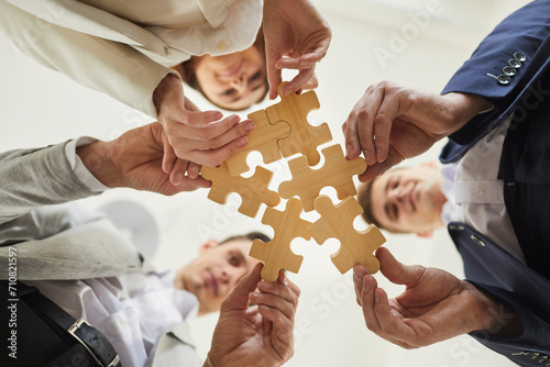 Business team trying to find solution to problem together. Group of young people holding parts of jigsaw puzzle. Crop shot close up bottom view from below hands holding wooden pieces. Teamwork concept