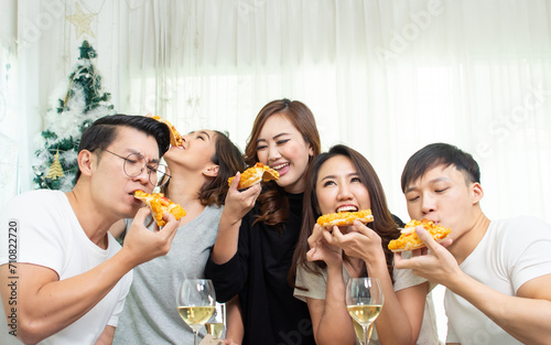 Group of five asian people or friend joining party in living room at home, talking and eating pizza together, smiling with happiness. Leisure, Lifestyle Concept.