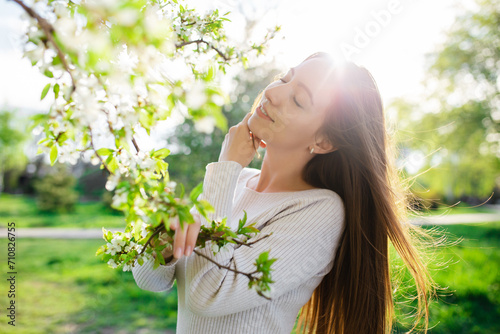 A beautiful young woman is posing, capturing the essence of spring, love, happiness, and femininity in a blossoming spring park at sunset. The setting conveys the joys of the season.