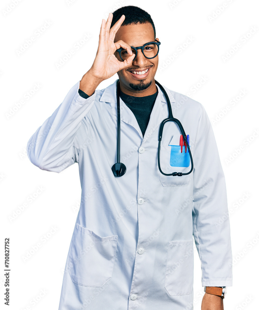 Young african american man wearing doctor uniform and stethoscope doing ok gesture with hand smiling, eye looking through fingers with happy face. Young african american man wearing doctor uniform and stethoscope doing ok gesture with hand smiling, eye looking through fingers with happy face.
