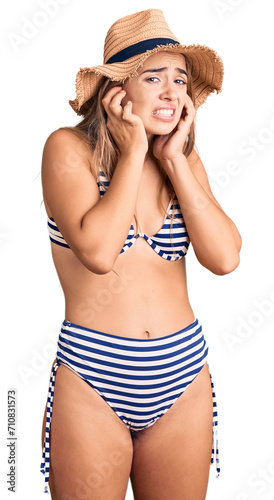 Young beautiful blonde woman wearing bikini and hat covering ears with fingers with annoyed expression for the noise of loud music. deaf concept. photo