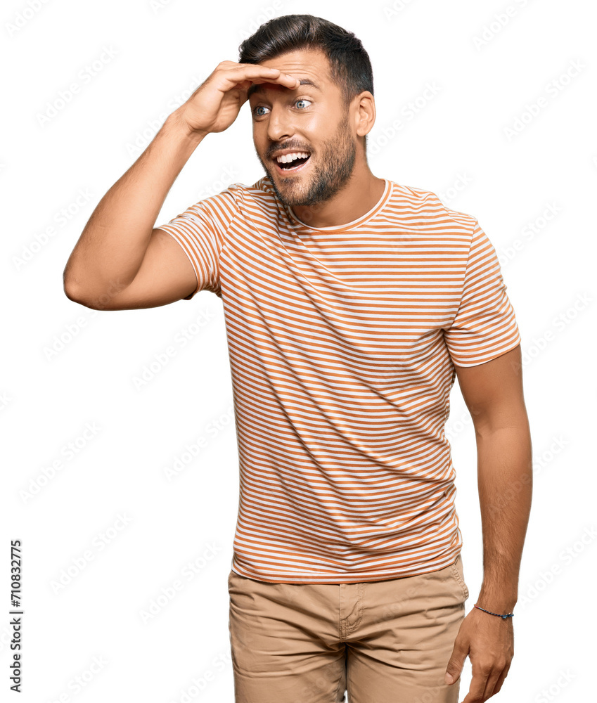Handsome hispanic man wearing casual clothes very happy and smiling looking far away with hand over head. searching concept.
