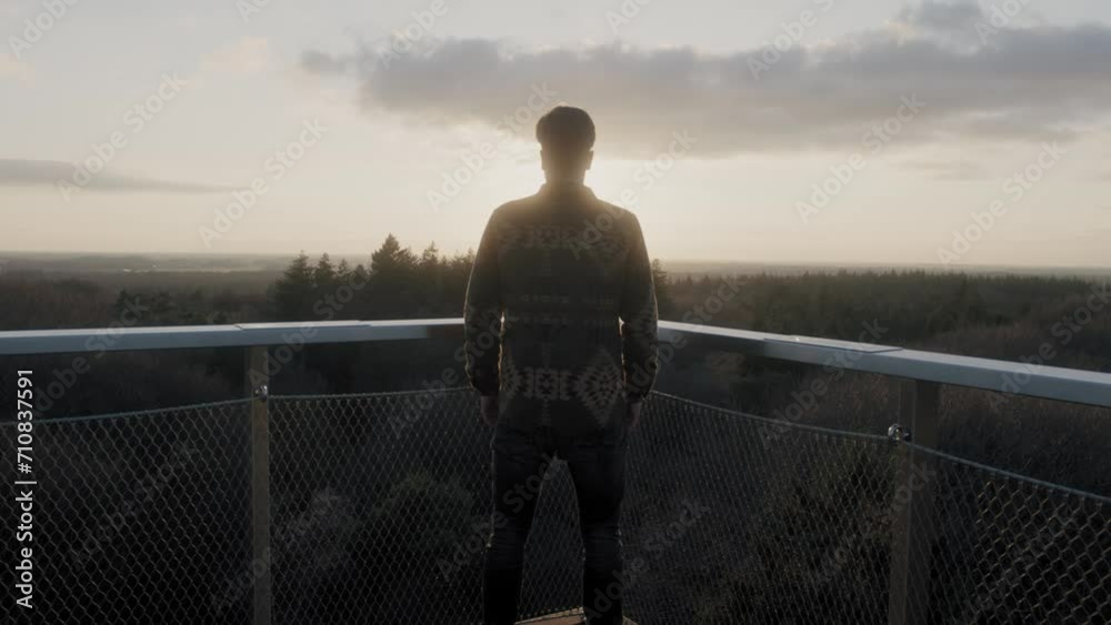 Man staring into a forest from a viewpoint during a sunset