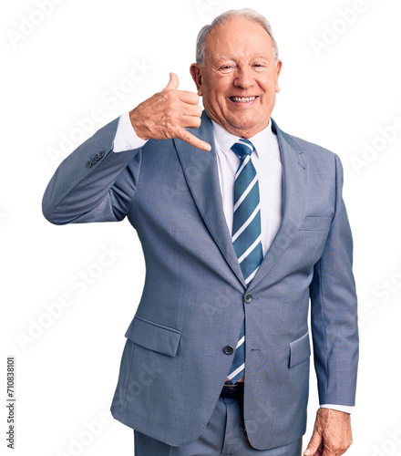 Senior handsome grey-haired man wearing elegant suit smiling doing phone gesture with hand and fingers like talking on the telephone. communicating concepts.