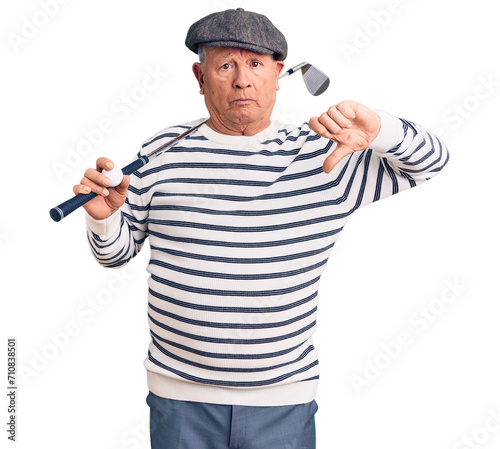Senior handsome grey-haired man holding golf club and ball with angry face, negative sign showing dislike with thumbs down, rejection concept