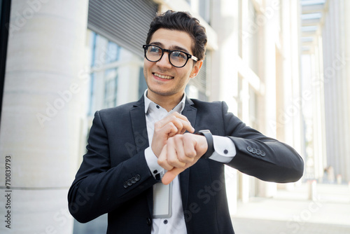 Smiling businessman checking smartwatch in urban setting. photo