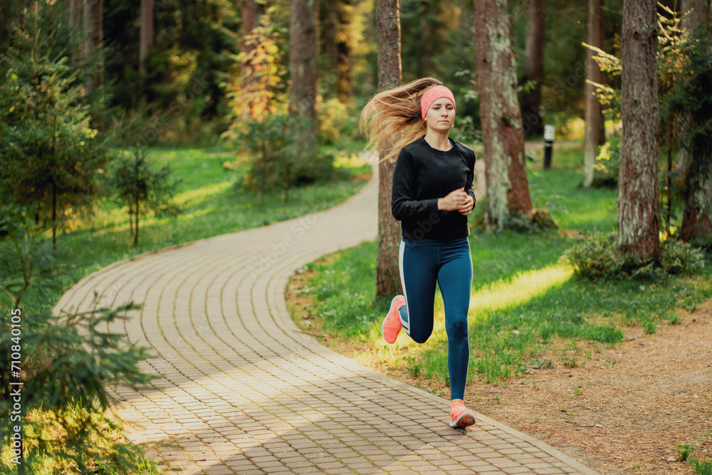 Female runner in vibrant sportswear jogging in a lush park at sunrise. Female runner in vibrant sportswear jogging in a lush park at sunrise.