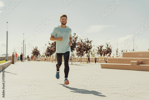 Man in a casual t-shirt jogging happily on a sunny waterfront promenade.