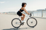 Stylish woman cycling on waterfront, enjoying urban life.