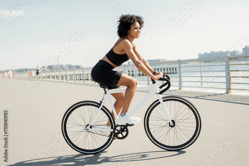 Stylish woman cycling on waterfront, enjoying urban life.