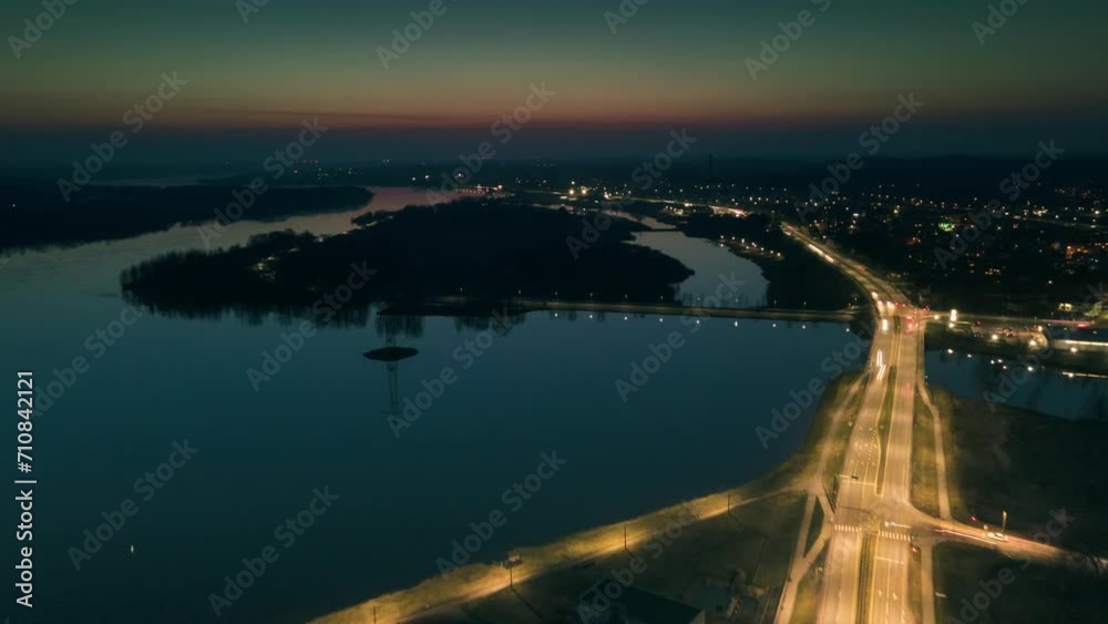 Aerial hyperlapse view of a small town in Latvia at dusk, traffic on a highway and reflection in the lake Aerial hyperlapse view of a small town in Latvia at dusk, traffic on a highway and reflection in the lake
