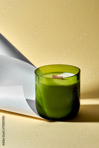 A minimalist composition of a candle in a jar and a paper on a yellow background. Aesthetic light