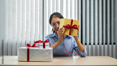 Young asian woman with many presents and holding gold gift box on her desk