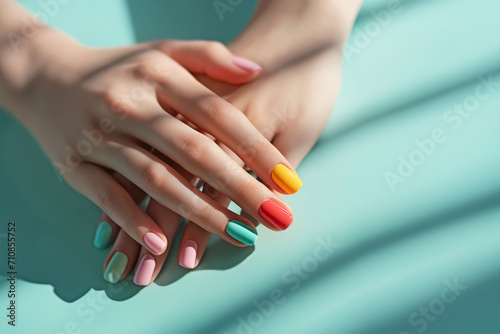 Female hands with pastel multicolored manicure elegantly crossed over a turquoise background photo