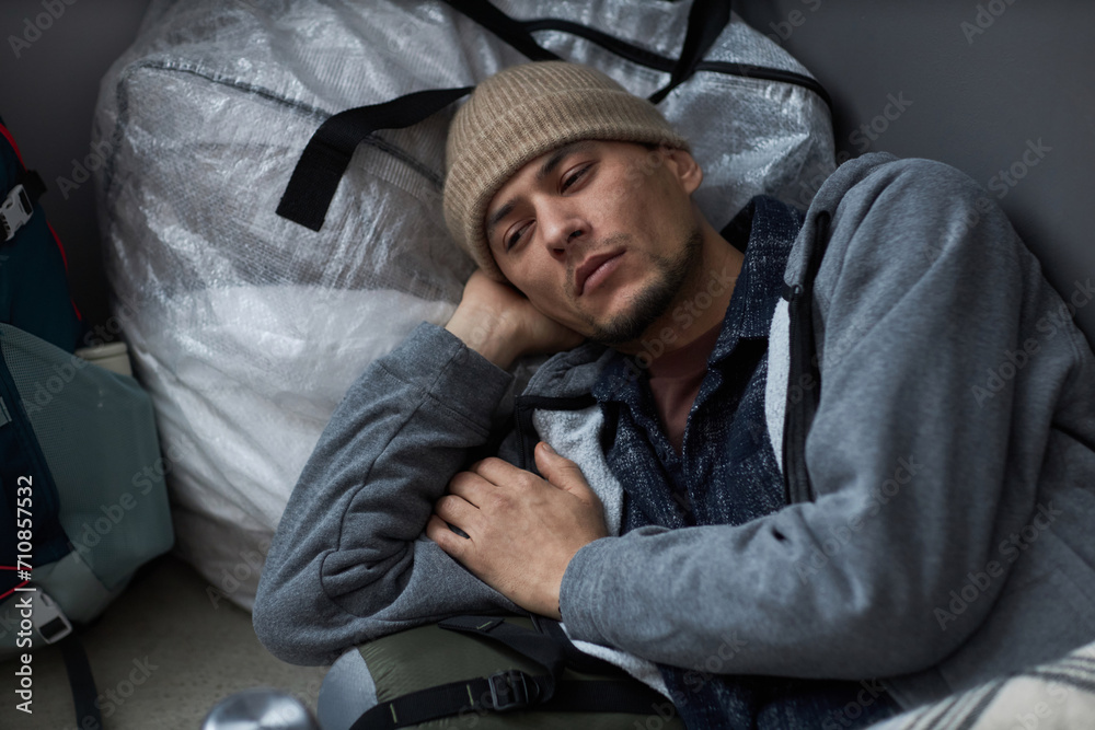 High angle portrait of Middle Eastern young man lying on floor at refugee shelter and looking away with sadness High angle portrait of Middle Eastern young man lying on floor at refugee shelter and looking away with sadness