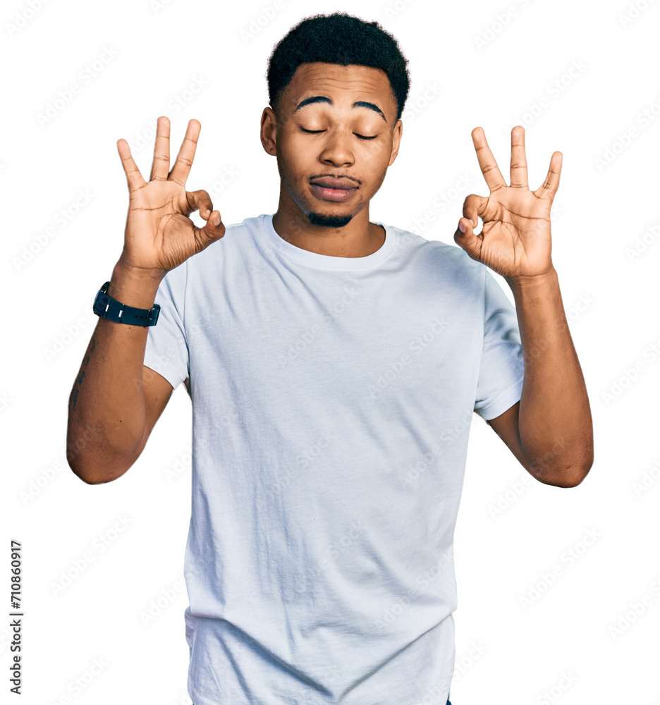Young african american man wearing casual white t shirt relaxed and smiling with eyes closed doing meditation gesture with fingers. yoga concept. Young african american man wearing casual white t shirt relaxed and smiling with eyes closed doing meditation gesture with fingers. yoga concept.
