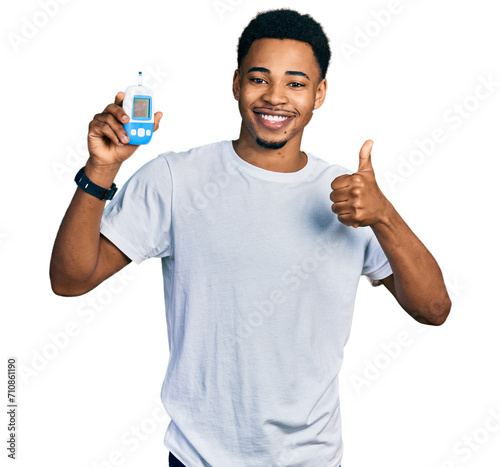 Young african american man holding glucometer device smiling happy and positive, thumb up doing excellent and approval sign photo