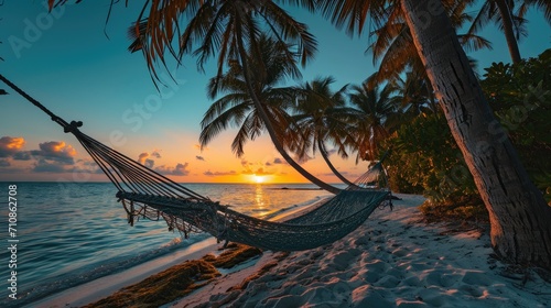 Beachside Relaxing Hammock Scene hung between palm trees on a tropical beach at sunset. © Thanaphon