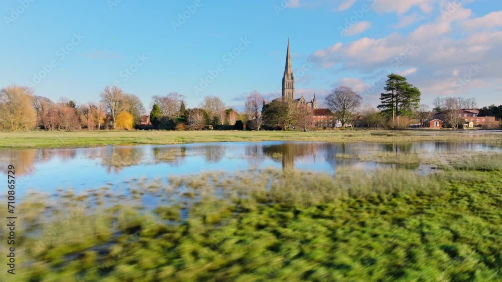 Low aerial shot flying fast over flooded fields with Salisbury cathedral in background reflected in water Low aerial shot flying fast over flooded fields with Salisbury cathedral in background reflected in water