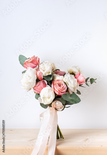 A designer bouquet of peonies, roses, eucalyptus, decorated with a ribbon, stands on a white background. Concept: gift for holiday, wedding, Valentine's Day