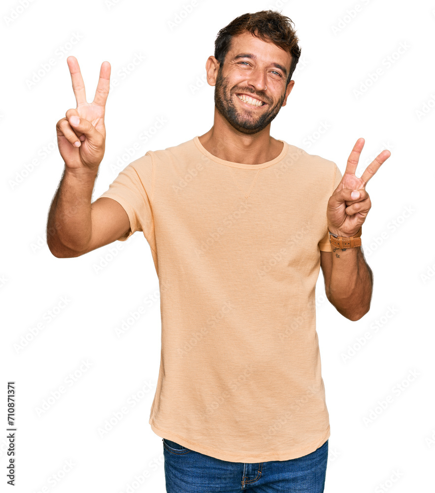 Handsome young man with beard wearing casual tshirt smiling with tongue out showing fingers of both hands doing victory sign. number two. Handsome young man with beard wearing casual tshirt smiling with tongue out showing fingers of both hands doing victory sign. number two.