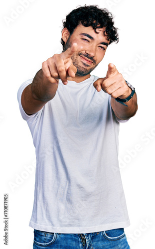 Hispanic young man with beard wearing casual white t shirt pointing to you and the camera with fingers, smiling positive and cheerful