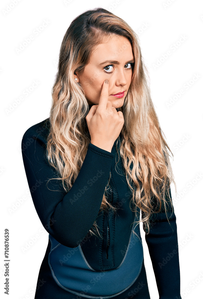 Young blonde woman wearing diver neoprene uniform pointing to the eye watching you gesture, suspicious expression Young blonde woman wearing diver neoprene uniform pointing to the eye watching you gesture, suspicious expression