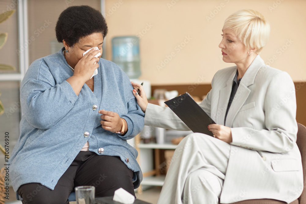 Fototapeta premium Portrait of depressed Black senior woman crying in therapy session with caring female psychologist