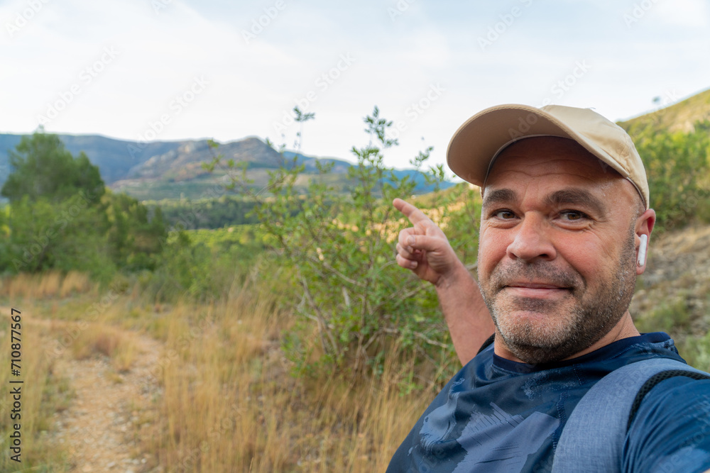 Hiker man takes a photo selfie in the mountain, pointing the landscape.