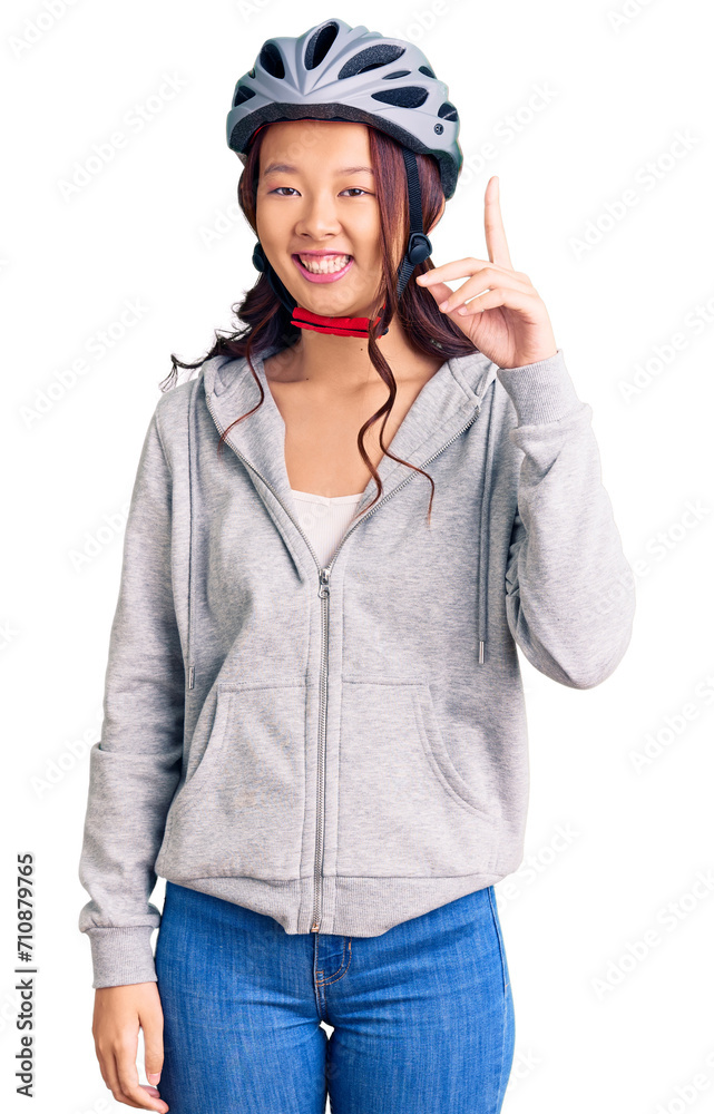 Young beautiful chinese girl wearing bike helmet pointing finger up with successful idea. exited and happy. number one. Young beautiful chinese girl wearing bike helmet pointing finger up with successful idea. exited and happy. number one.