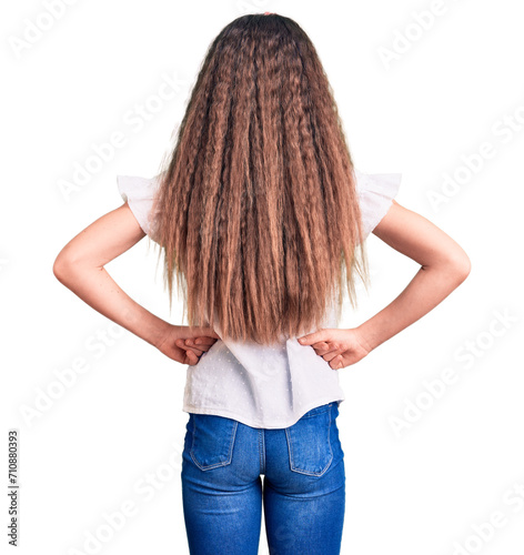 Cute hispanic child girl wearing casual white tshirt standing backwards looking away with arms on body