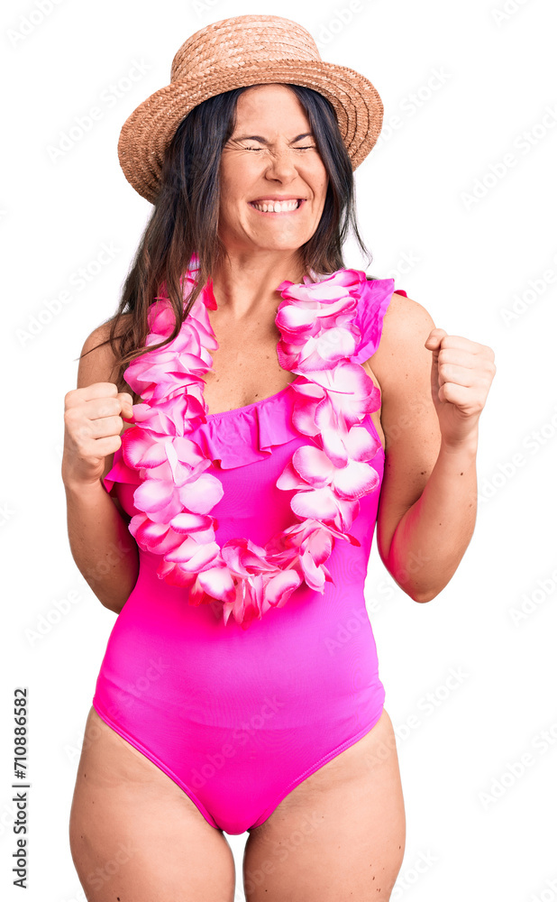 Young beautiful brunette woman wearing swimwear and hawaiian lei excited for success with arms raised and eyes closed celebrating victory smiling. winner concept. Young beautiful brunette woman wearing swimwear and hawaiian lei excited for success with arms raised and eyes closed celebrating victory smiling. winner concept.