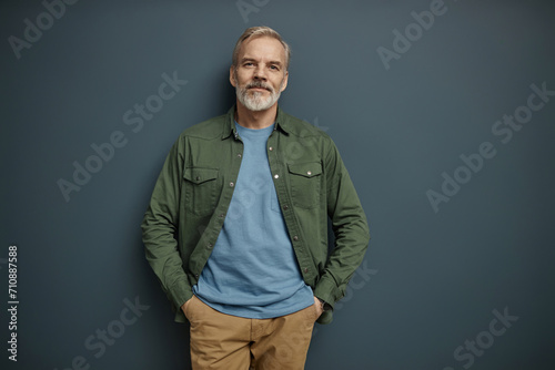Waist up portrait of bearded mature man looking at camera against grey background, copy space