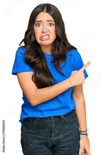 Beautiful brunette young woman wearing casual clothes pointing aside worried and nervous with forefinger, concerned and surprised expression